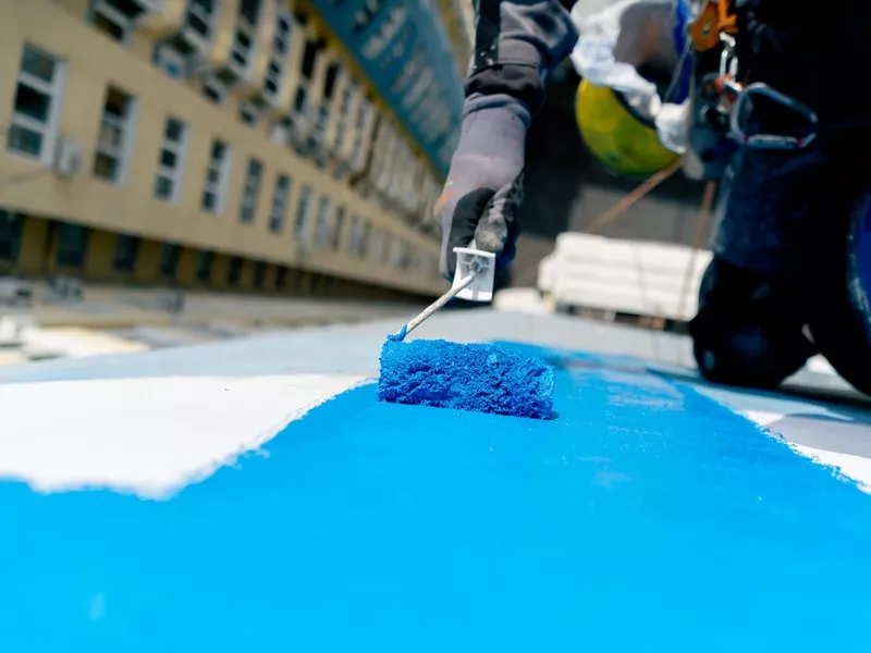 Professional roofer applying a protective blue liquid roof coating to a commercial flat roof for waterproofing and energy efficiency.