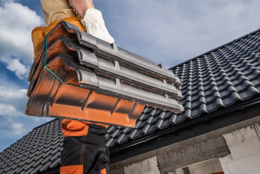 A professional roofer carrying a fresh bundle of grey roof tiles at a residential construction site for a complete roof replacement project.