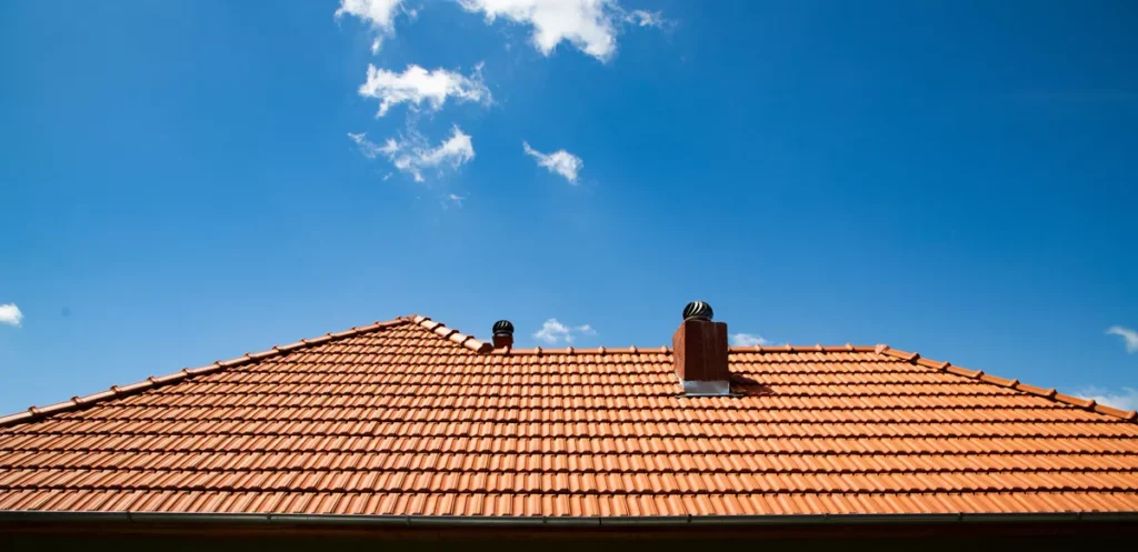 A high-angle view of a traditional red terracotta tile roof with chimneys under a clear blue Scottsdale sky, showcasing heat-resistant residential roofing.