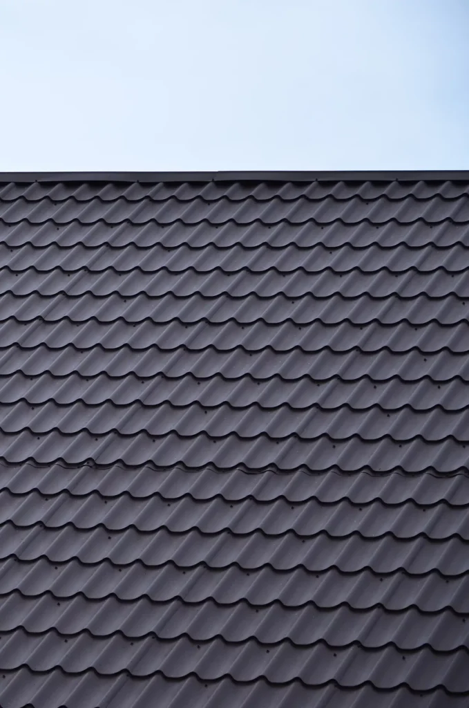 A close-up of a perfectly aligned gray undulating tile roof against a clear sky, showcasing the precision and pattern of a professional residential installation.