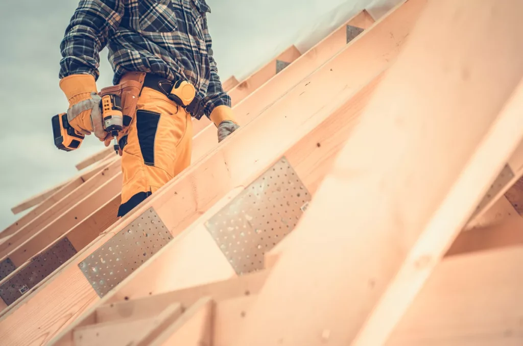 A skilled roofing contractor using a power drill to secure wooden roof trusses and metal braces during a residential new construction project in Scottsdale.